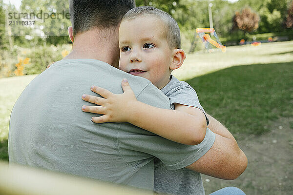 Boy embracing father with arm around in playground