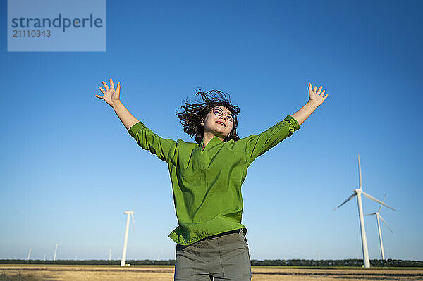 Happy young woman jumping with arms raised under blue sky