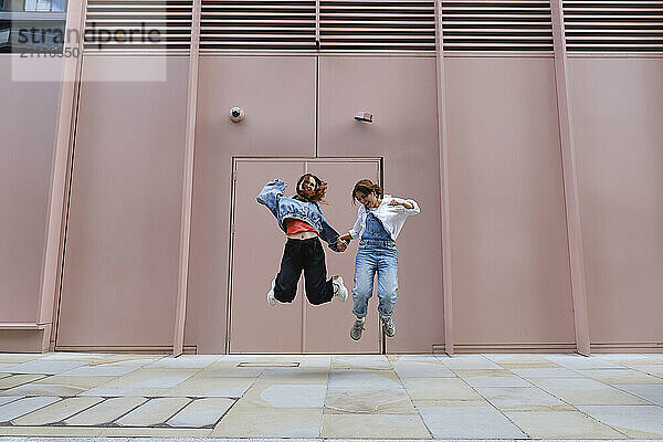 Gay couple jumping on sidewalk in front of pink building