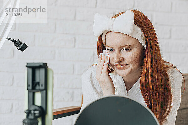 Teenage girl using facial cleanser during skincare routine while vlogging at home.