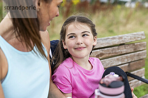 Smiling girl sitting with mother on bench