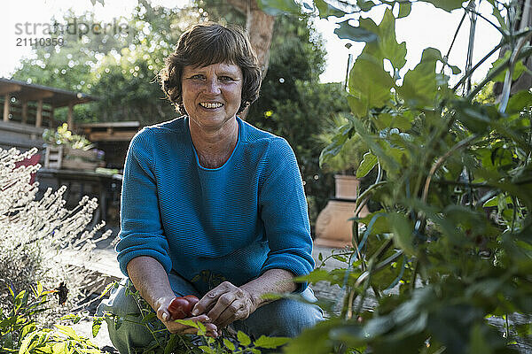 Happy senior woman with tomatoes in back yard