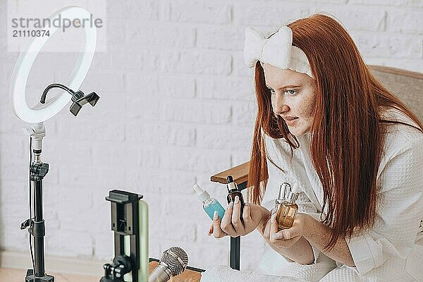 Teenage beauty vlogger filming a skincare product review at home using a ring light and microphone.