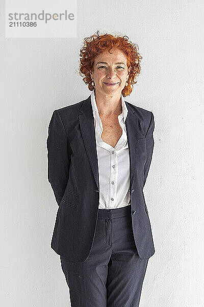 Smiling businesswoman with hands behind back standing against white background