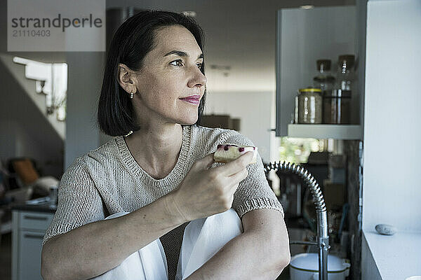 Woman holding slice of cake and sitting in kitchen at home