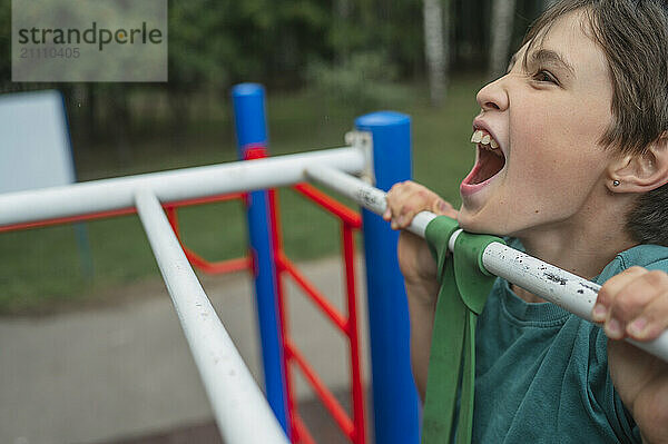 Playful boy holding on play equipment at park