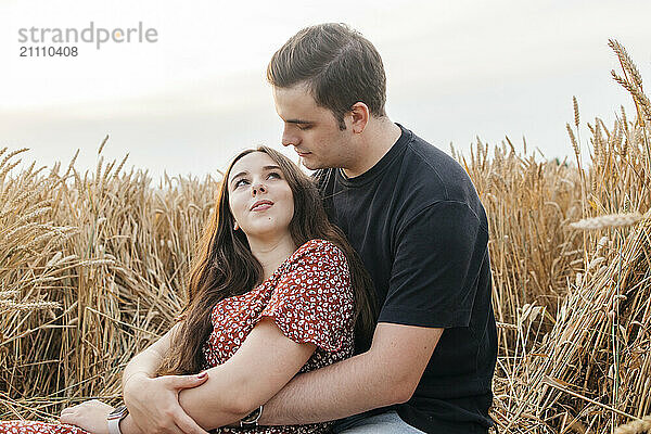 Affectionate young man sitting and embracing girlfriend amidst agricultural field