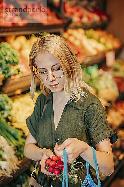 Blond woman buying radishes at vegetable stall