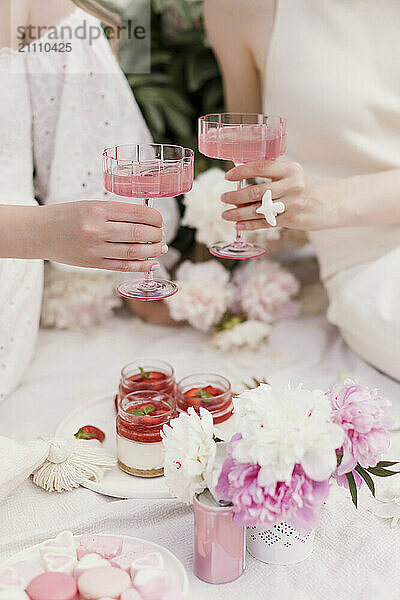 Friends doing celebratory toast with pink lemonade sitting on picnic blanket