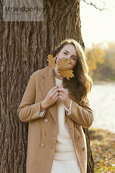 Woman covering face with maple leaf at forest