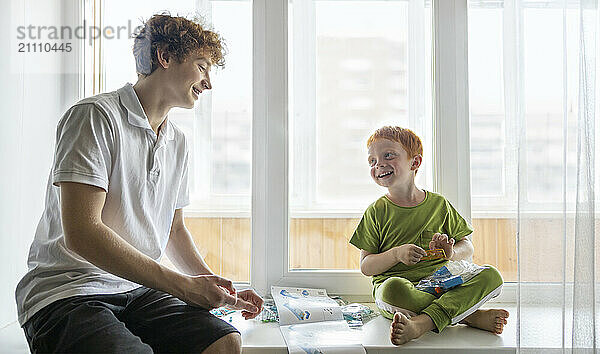 Happy boy sitting with brother on window sill at home