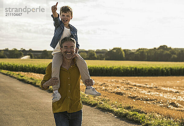 Cheerful boy enjoying sitting on grandfather's shoulder