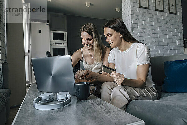 Friends doing online shopping with credit card on laptop at home