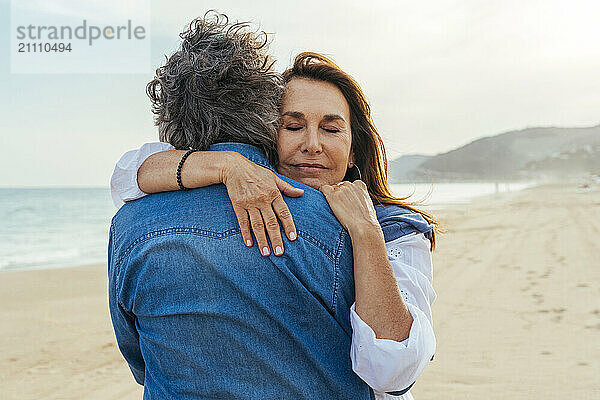 Smiling senior woman hugging man at beach