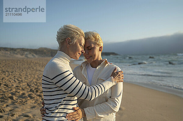 Affectionate mother embracing daughter on beach at sunny day