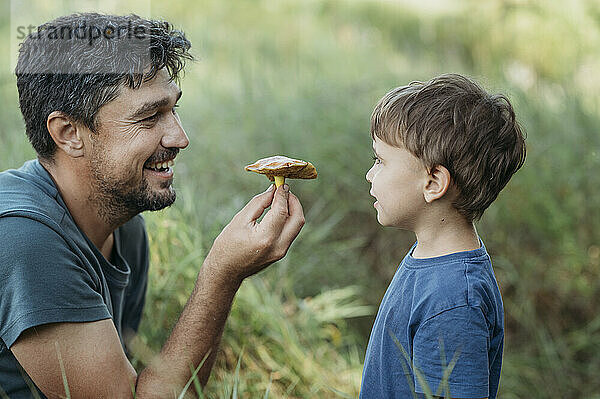 Happy father showing mushroom to son at forest