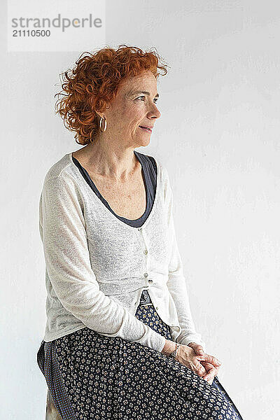 Thoughtful redhead woman sitting against white background