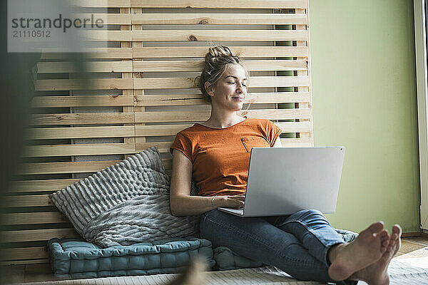 Portrait of woman sitting on mattress relaxing with laptop