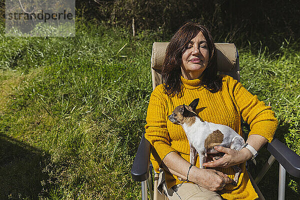 Senior woman sitting on camping chair with dog at sunny day