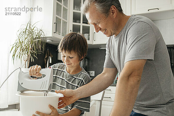 Happy father with son using electric mixer in kitchen