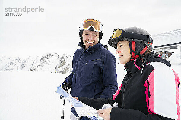 Happy man and woman standing with map in winter