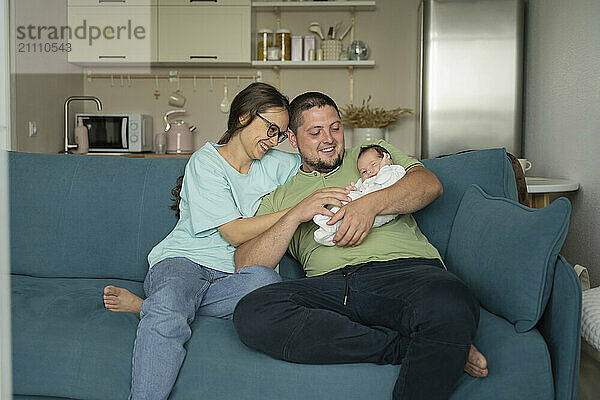 Mother and father embracing baby sitting on sofa at home