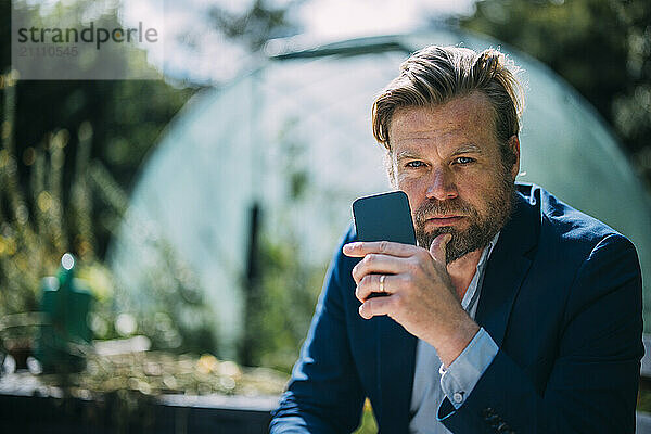 Confident businessman holding smart phone at sunny day