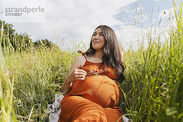 Pregnant woman sitting near grass under sky