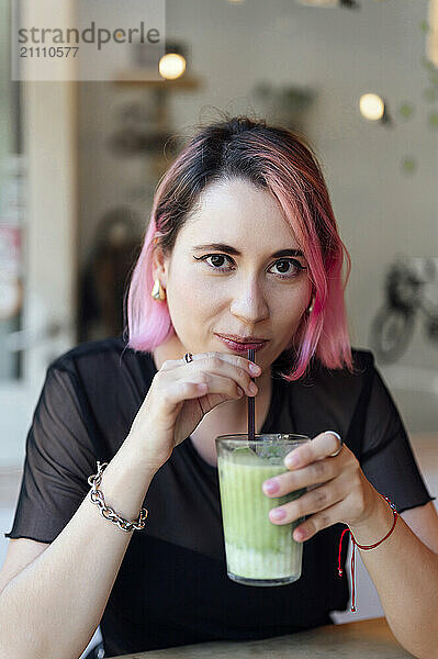 Woman with pink hair drinking matcha tea at cafe