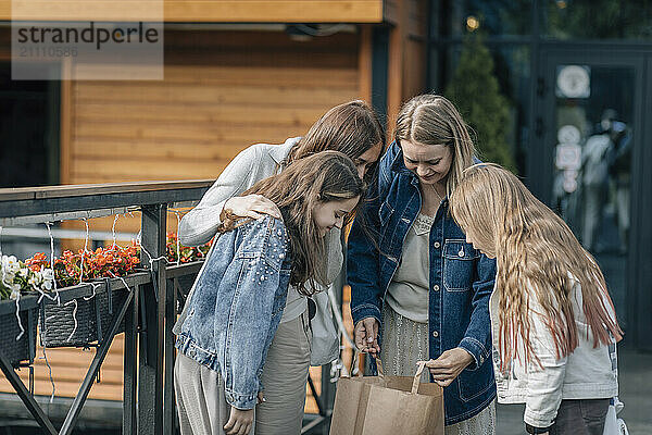 Mothers with daughters holding shopping bag and standing outside store