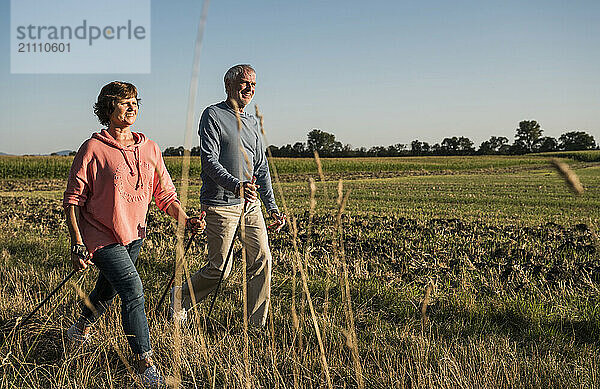 Smiling senior couple walking with hiking poles near field