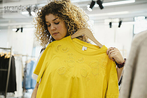 Young woman with curly hair shopping for clothes indoors in a trendy retail store.