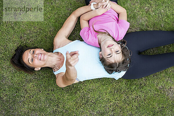 Woman pointing at sky lying down with daughter on grass in back yard