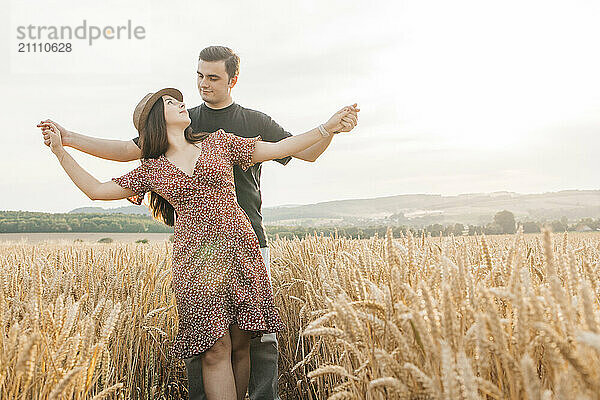 Romantic couple standing with arms outstretched in agricultural field