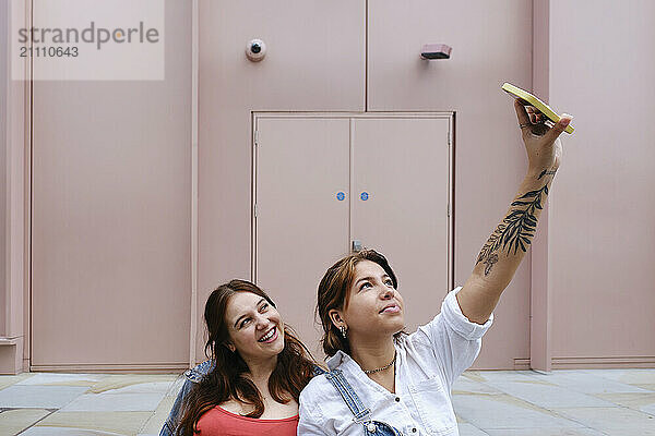 Young gay couple taking selfie in front of building near footpath