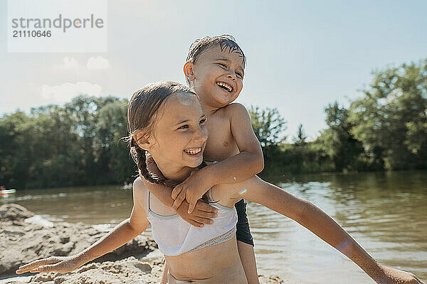 Smiling girl giving piggyback ride to brother near river