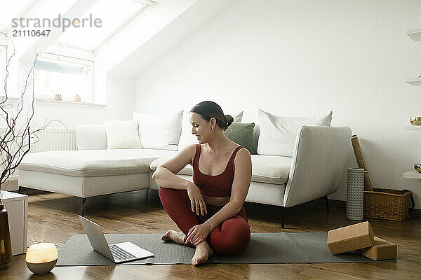 Smiling woman watching exercise tutorial on laptop at home