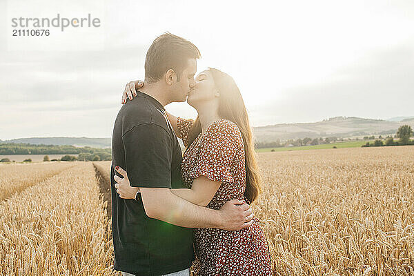 Romantic couple kissing in agricultural field at sunset