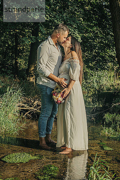 Couple kissing and standing on stream near forest