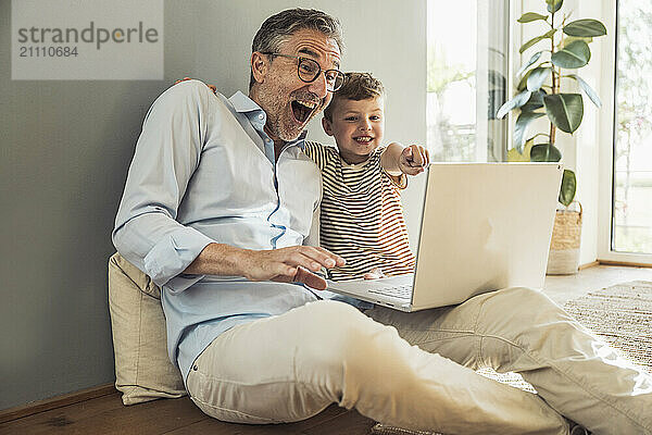 Happy grandfather and grandson enjoying using laptop at home