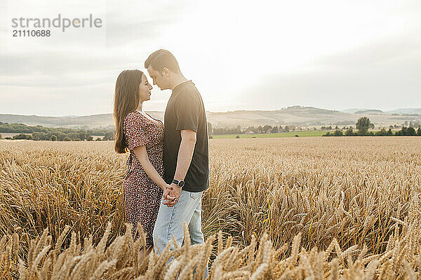 Romantic couple standing face to face and holding hands amidst agricultural field