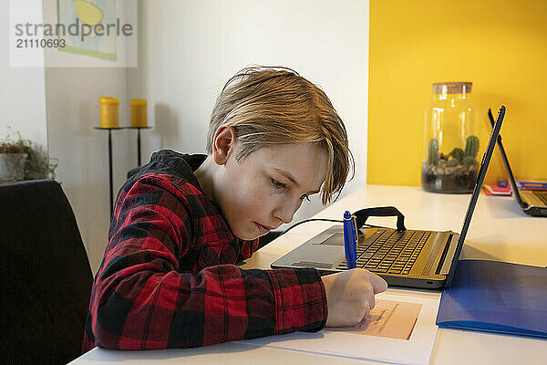 Boy doing homework with laptop on table at home