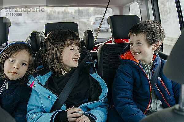 Happy siblings in warm clothes traveling by car