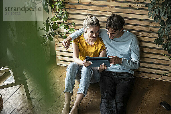 Young man with arm around girlfriend using tablet PC and sitting at home