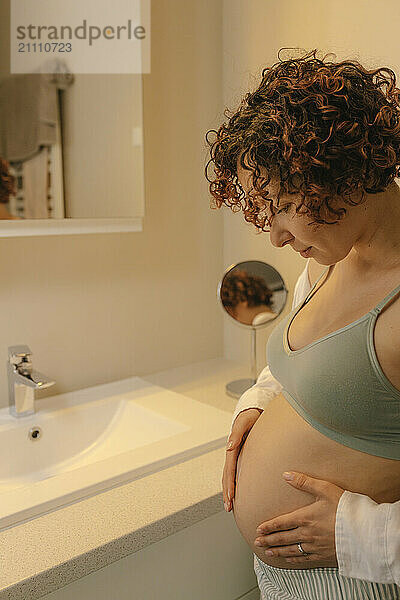 Pregnant woman looking down and smiling in the bathroom.