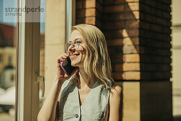 Smiling beautiful blond woman talking on smart phone at sunny day