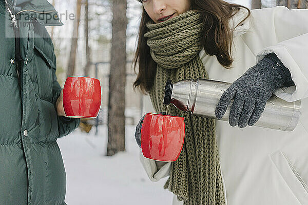 Woman in warm clothes pouring coffee in cups