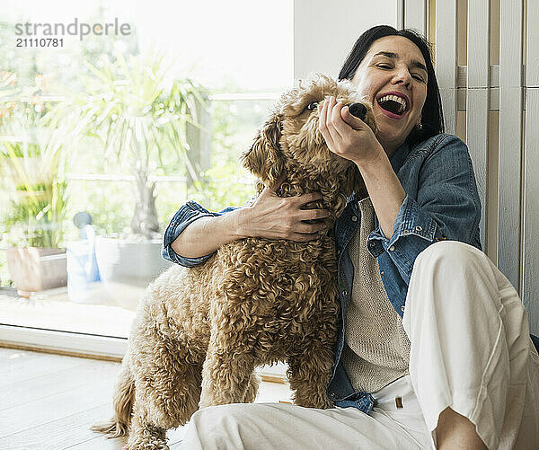 Cheerful woman playing with dog at home