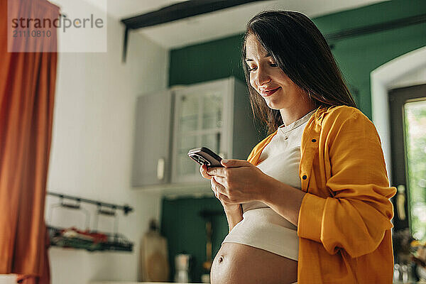 Smiling pregnant woman using smart phone at home