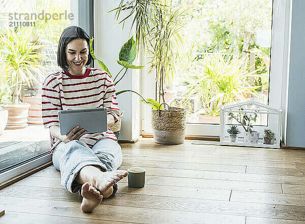 Smiling woman using tablet PC sitting near plants at home